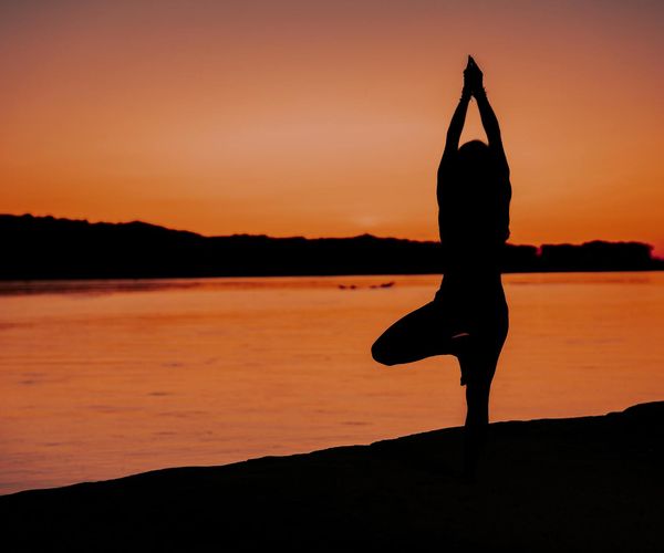 Silhouette of a person in a yoga tree pose at sunset.